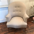 French vintage tub chair covered in Taupe linen with a buttoned back, beechwood cabriolet legs and brass castors. Late 19th C.